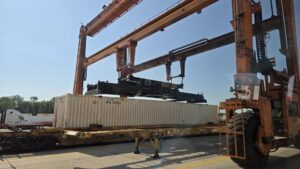 An overhead rubber tire crane moves a trailer in position.